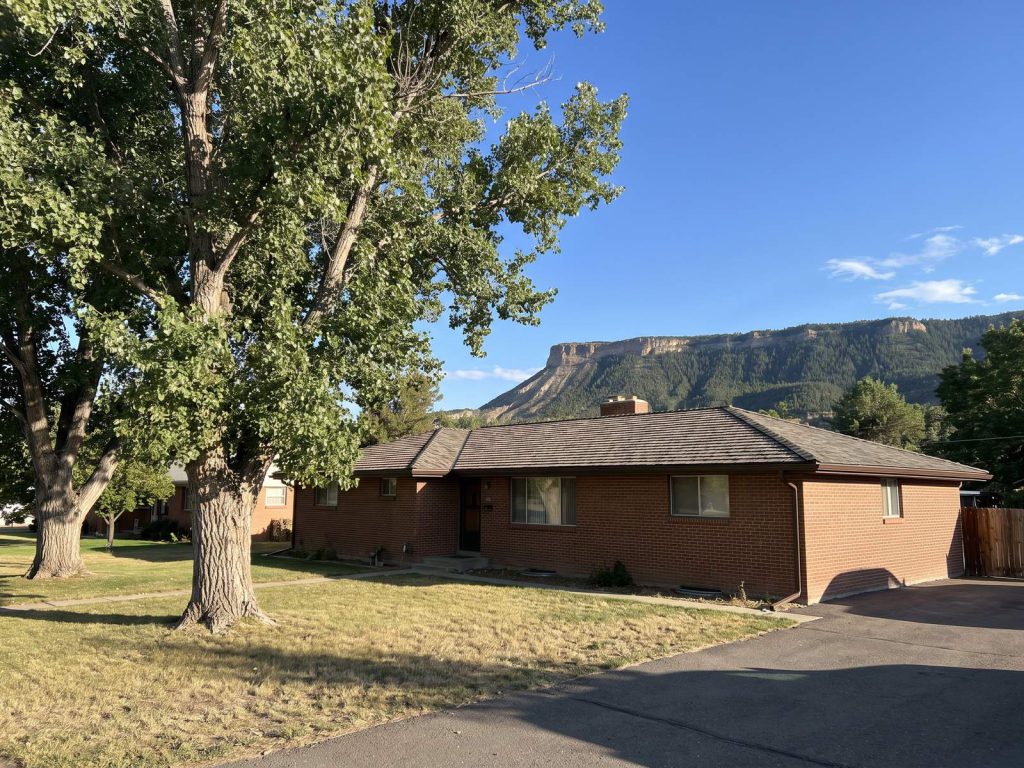 Brick ranch home with a new shingle roof under cottonwoods and a distant mesa