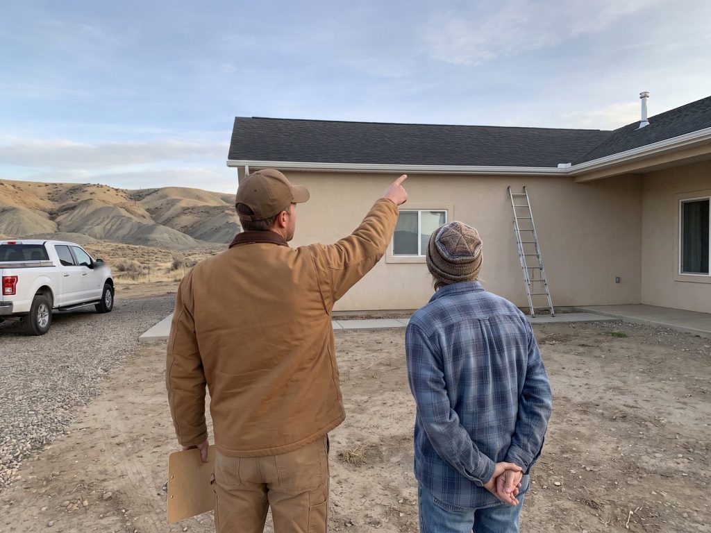 Roofer and homeowner seen from behind looking over a roof together