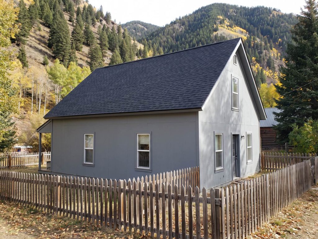 Older gabled mountain-town house with a new roof below steep forested slopes
