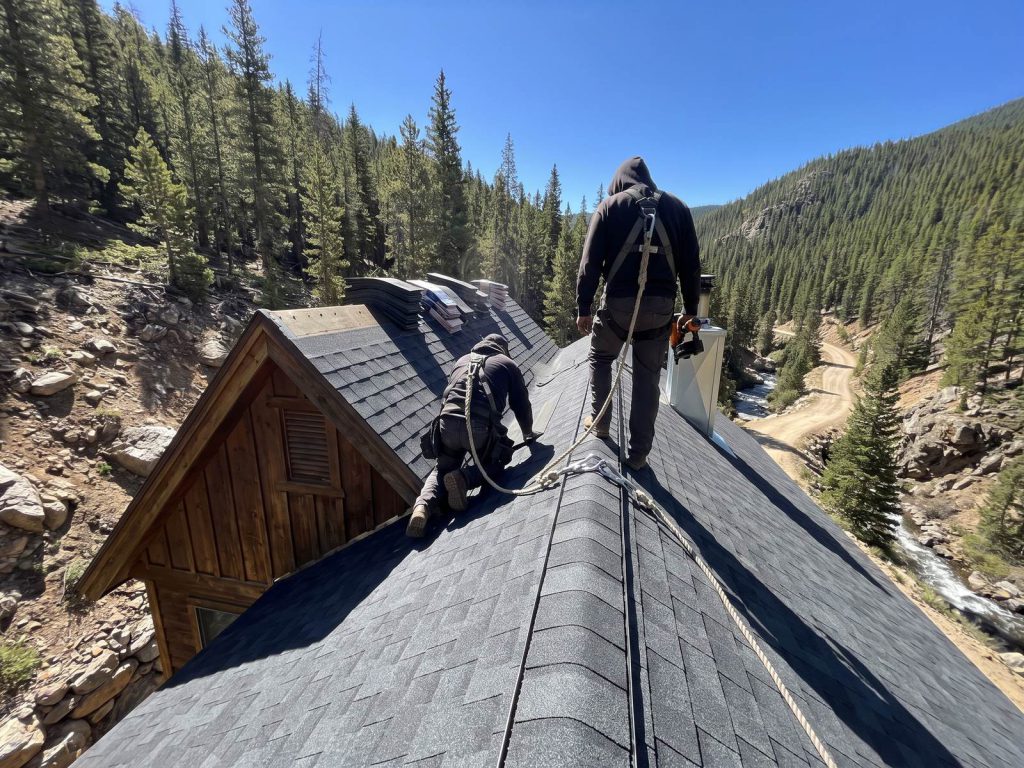 Roofers in harnesses on a steep mountain home roof in a forested canyon