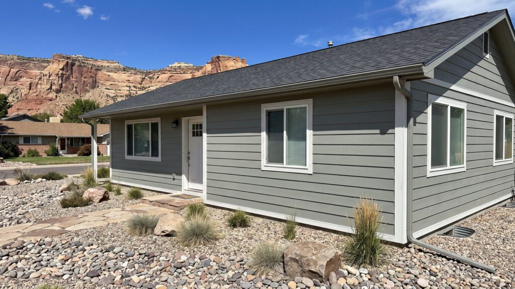 A ranch home re-sided in sage-gray fiber cement lap siding with white trim, red rock cliffs behind