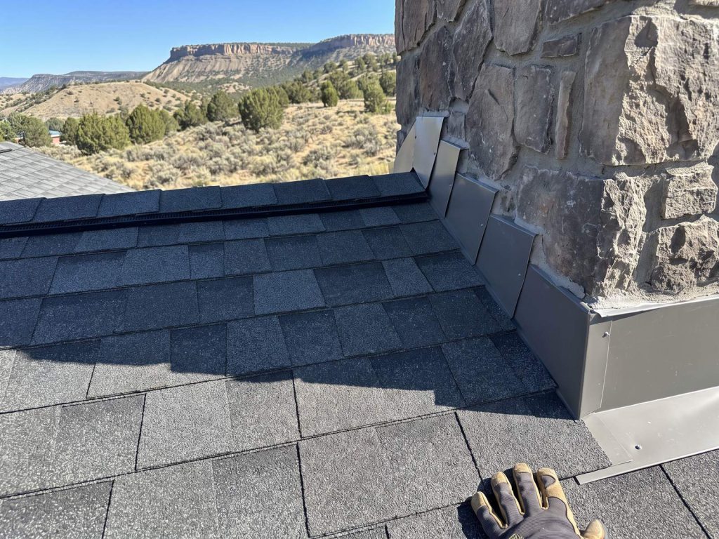 New shingles with clean step flashing at a chimney, cliffs and sagebrush hills beyond