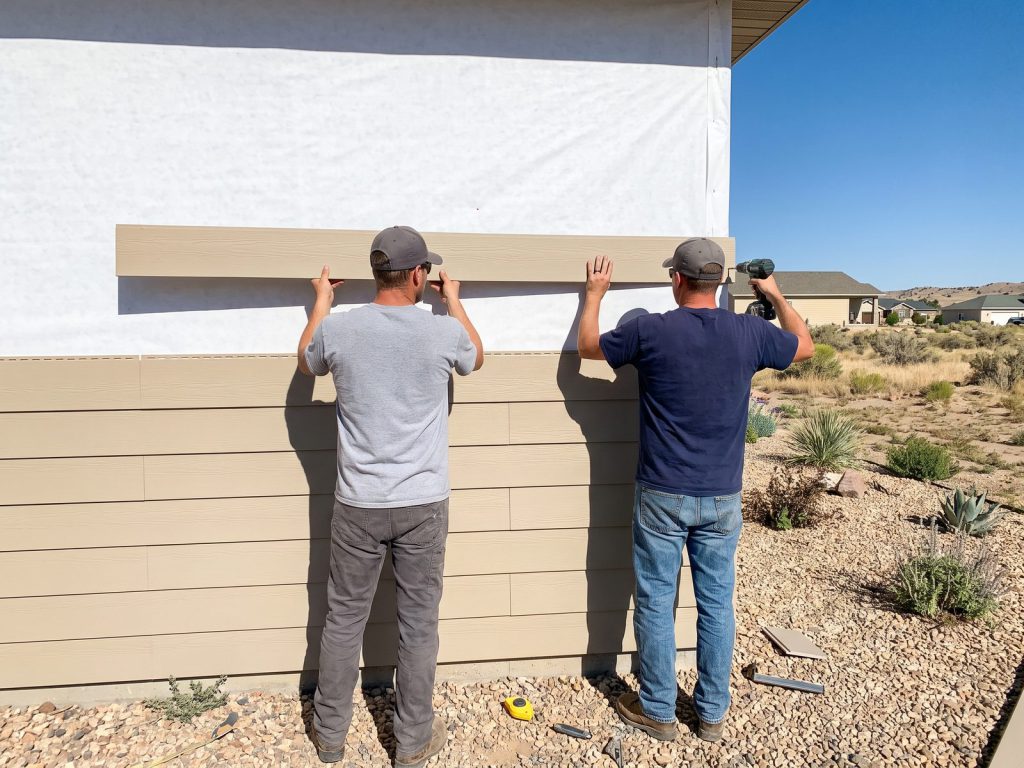 Two installers seen from behind fastening new lap siding on a ranch home