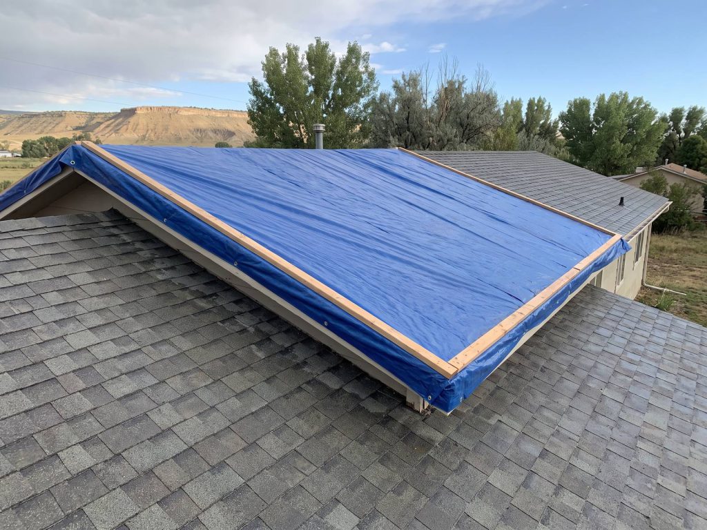 Blue tarp secured with wood battens over a storm-damaged shingle roof